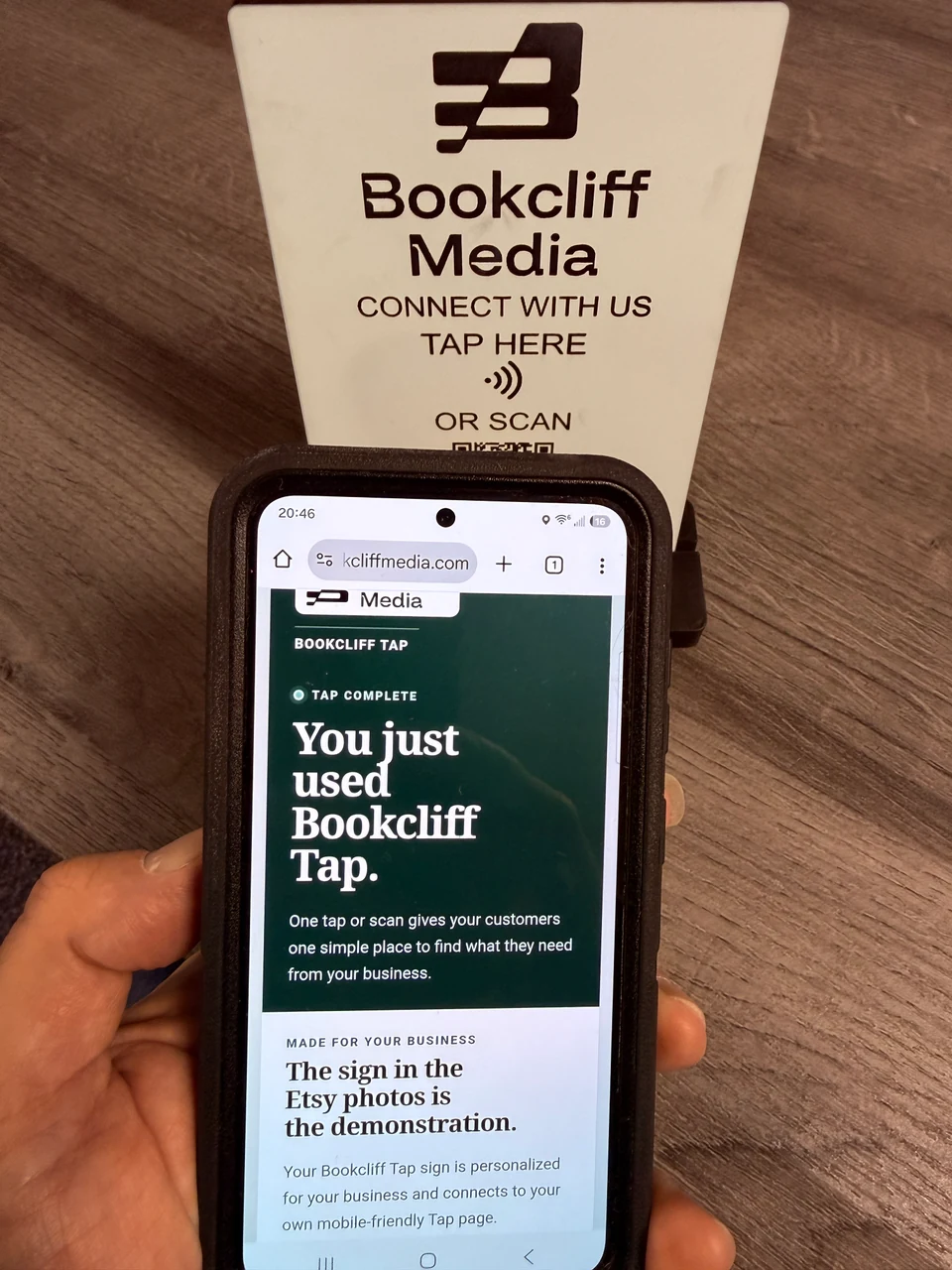 Bookcliff Tap Page opened on a phone beside an acrylic Tap Sign